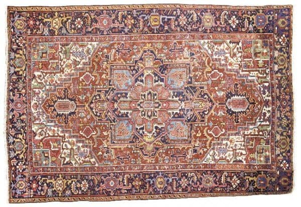Lot 22 – A Heriz carpet, North-West Persia. The shaded rust field with angular palmette and leafy vine around stepped indigo medallion with hooked palmette pendants containing palmette cartouches enclosing dusty-pink radiating floral centrepiece, ivory spandrels similar, in broad shaded indigo border of bold polychrome turtle-palmettes and angular floral vine between shaded brick-red floral meander stripes, very slight (secured) loss at each end, slight wear.